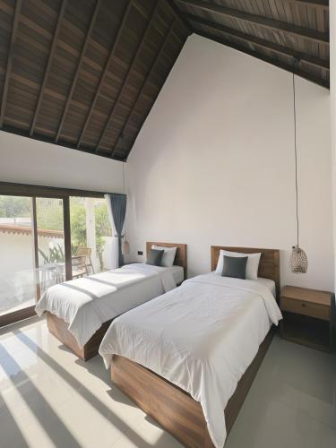 two beds in a bedroom with white walls and windows at Ginantary Cottages in Uluwatu