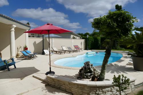 ein Pool mit einem roten Regenschirm und einem Baum in der Unterkunft Les Hortensias Du Monastère in Saint-Aubin-de-Médoc
