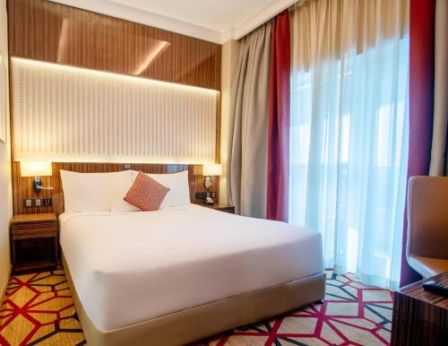 a bedroom with a large white bed and a television at Naumi Hotel Dubai in Dubai