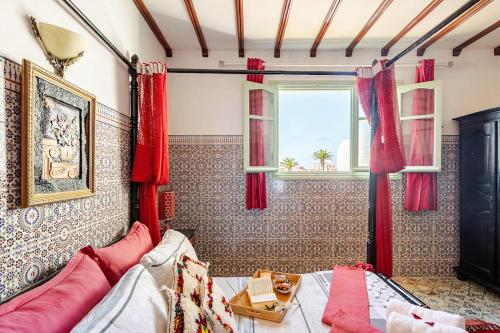 アル・ジャディーダにあるVue sur mer Riad Statia Votre refuge authentiqueの赤いカーテンとベッド、窓が備わるベッドルーム1室が備わります。