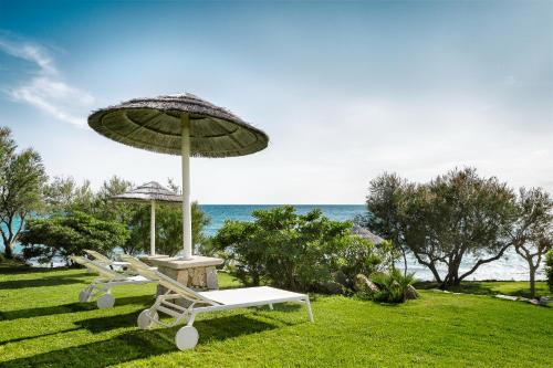 a chair and an umbrella on the grass near the ocean at Hotel Stella Maris in Villasimius