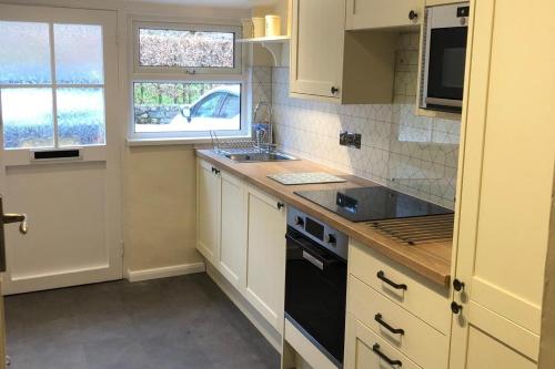 a kitchen with white cabinets and a black stove top oven at Talcomb Cottage in Thornthwaite Keswick in Keswick