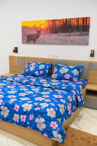 a bed with a blue comforter with a deer painting on the wall at CHROME Résidences Fidjrossè PLAGE in Cotonou