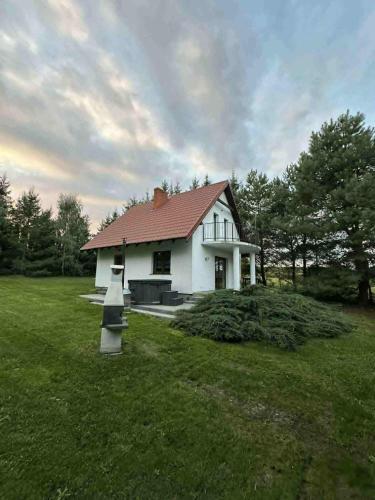 a white house with a red roof in a field at Domek nad Jeziorem z Jacuzzi na Mazurach 10os in Jedwabno