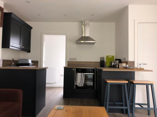 eine Küche mit schwarzen Schränken und einer Theke mit Stühlen in der Unterkunft Apartment Bushmills Hideaway Parking Pets Allowed in Bushmills