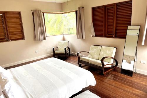 a bedroom with a bed and two chairs and a window at Pear Tree House Barbados in Saint James