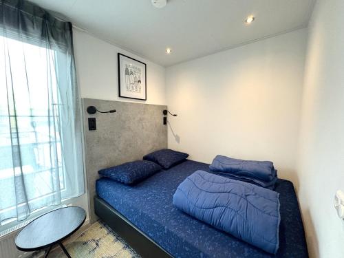 a bedroom with a bed with blue sheets and a window at De Maasterp - Woonboot 5 in Montfort