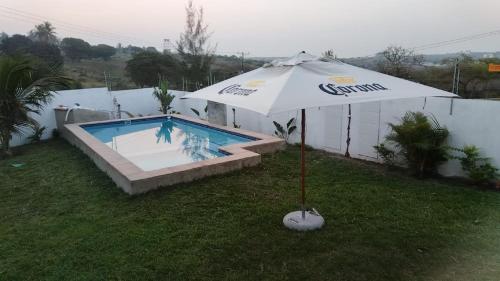 an umbrella sitting in the grass next to a swimming pool at Eulália villa in Vila Praia Do Bilene