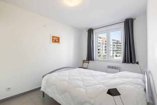 a white bedroom with a bed and a window at Plaza in Sint-Idesbald