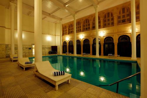 a swimming pool with two lounge chairs and a large building at The Lallgarh Palace - A Heritage Hotel in Bikaner