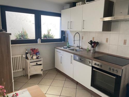 a kitchen with white cabinets and a sink and two windows at Schöne Ferienwohnung mit Ausblick in die Natur in Kierspe