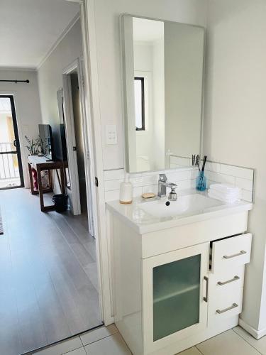 a white bathroom with a sink and a mirror at Sunny Tidy Corner in Ellerslie in Auckland