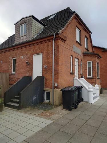 a brick house with a white door and a fence at Lejlighed med højt til loftet in Herning