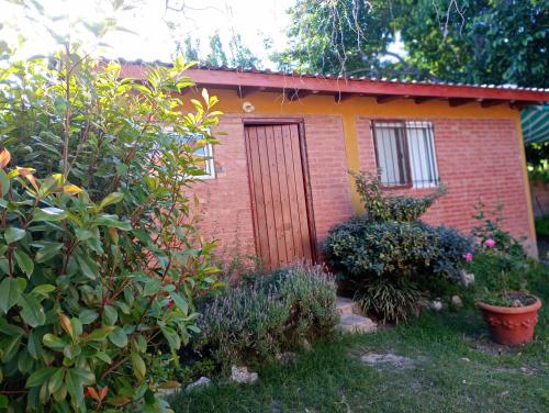 a small brick house with a door in a garden at Casa Sol Y Rio in Mina Clavero