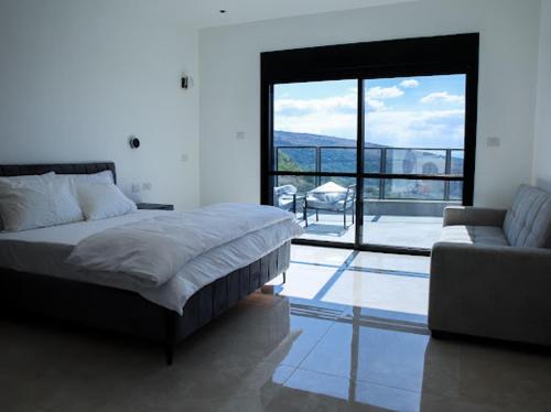 a bedroom with a bed and a couch and a large window at Vista royal golan in Ein Kinya
