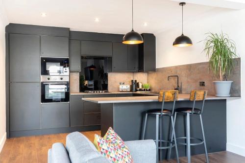 una cocina con armarios grises y taburetes de bar en Central 2-Bed Modern Home with Garage, en Cheltenham