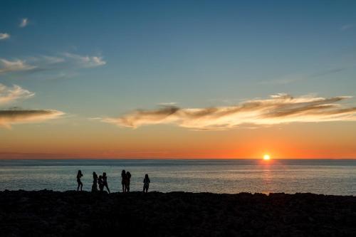 a group of people standing on a beach at sunset at Apartamentos Blancala in Cala Blanca