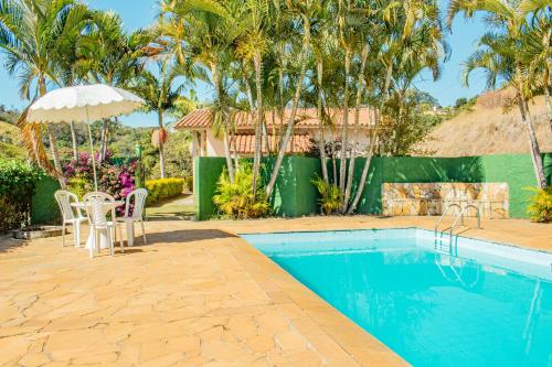 a pool with chairs and an umbrella and palm trees at Parque Pousada Macaquinho Turismo in Serra Negra