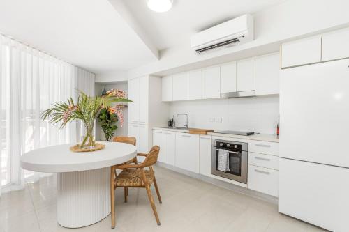 a white kitchen with a table and chairs at Luxe at Oshen Yeppoon in Yeppoon