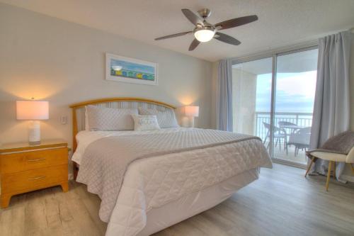 a bedroom with a bed with a ceiling fan and a balcony at Crescent Shores North - 502 in Myrtle Beach