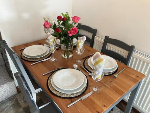 a wooden table with plates and a vase of roses at Character Cottage in Usk in Usk
