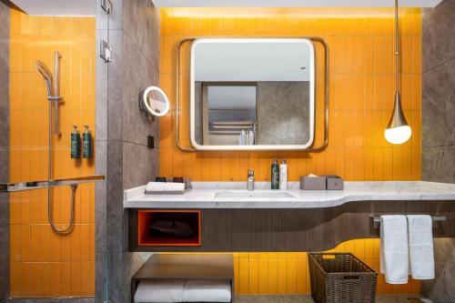 Baño de color naranja con lavabo y espejo en Home2 Suites by Hilton Zhangjiajie Tianmen Mountain, en Zhangjiajie