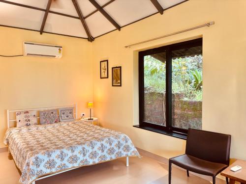 ein Schlafzimmer mit einem Bett, einem Fenster und einem Stuhl in der Unterkunft The Lookout, Hilltop Cottage in Curtorim