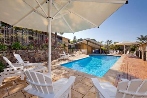 a pool with white chairs and an umbrella at Tathra Beach House Holiday Apartments in Tathra