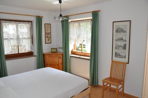 a bedroom with green curtains and a bed and a chair at Casa Guido e Laura in Pozza di Fassa