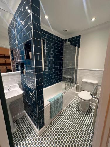 ein Badezimmer mit Toilette und Waschbecken und blauen Fliesen in der Unterkunft Life's A Beach - cosy, luxury cottage in Ashley Cross, Poole in Parkstone