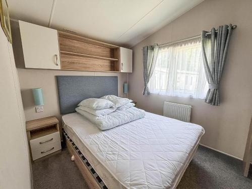 a small bedroom with a bed and a window at 6 Berth Caravan With Stunning Sea Views And Decking To Relax On, Ref 32048Az in Lowestoft