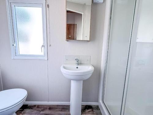 a white bathroom with a sink and a toilet at 6 Berth Caravan With Stunning Sea Views And Decking To Relax On, Ref 32048Az in Lowestoft