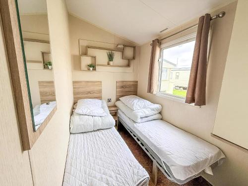 two beds in a small room with a window at Great Caravan With Central Lounge & Wifi At Broadland Sands, Suffolk Ref 20070Bs in Hopton on Sea