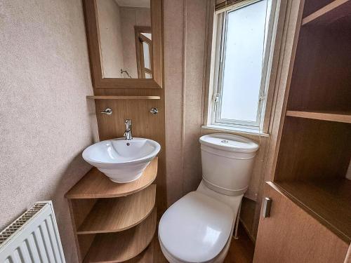 a bathroom with a toilet and a sink and a window at Lovely 6 Berth Caravan With Decking At California Cliffs In Scratby Ref 50048L in Great Yarmouth