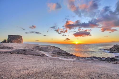 una puesta de sol sobre el océano con un faro en una playa en Casa Marinera El Cotillo duplex for 2-4 persons, en Cotillo