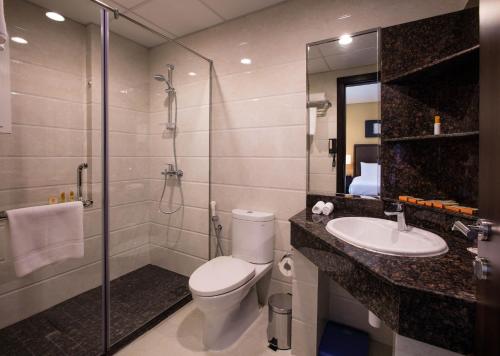 a bathroom with a toilet and a shower and a sink at Orange Suites Hotel in Manama