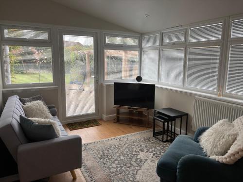 a living room with a couch and a television and windows at The Corner House, 36, Broadway Road, in Evesham