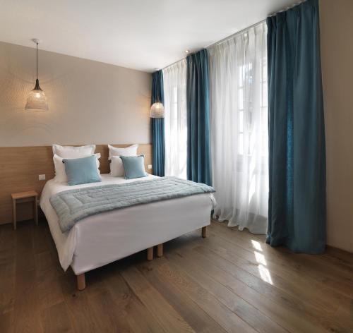 a bedroom with a large bed with blue curtains at Hôtel Beau Site Talloires B SPA in Talloires