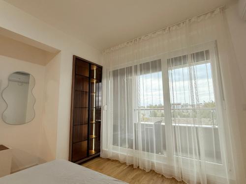 1 dormitorio con una gran ventana con cortinas blancas en Apartment UNA, en Pančevo