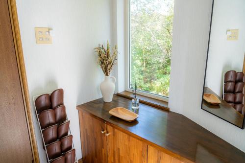 een kamer met een vaas op een houten dressoir met een raam bij ウィステリア in Teshikaga