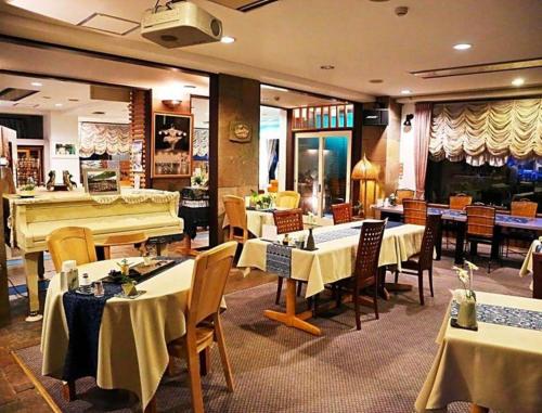 白馬村にあるOkanoue Hotel Miyagawaのテーブルと椅子、グランドピアノのあるレストラン