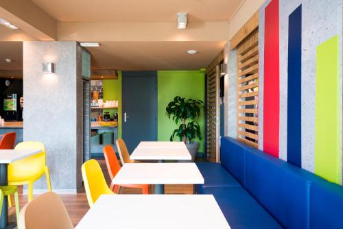 a restaurant with white tables and colorful chairs at ibis budget Granville in Granville