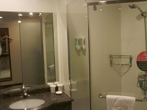 a bathroom with a sink and a glass shower at GreenTree Inn Heze Railway Station Hotel in Heze