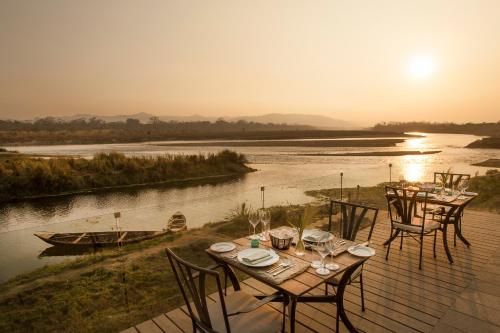 a table and chairs on a deck next to a river at Meghauli Serai Chitwan National Park - A Taj Safari Lodge in Meghauli