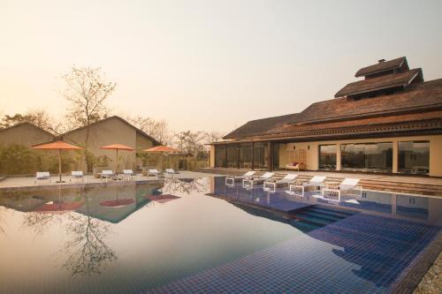 a swimming pool with white chairs and a building at Meghauli Serai Chitwan National Park - A Taj Safari Lodge in Meghauli