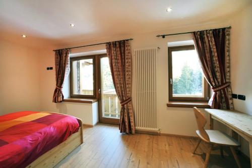 a bedroom with a bed and a desk and windows at Appartamenti da Nica e Diego in Borca di Cadore
