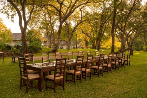 a long wooden table and chairs in a park at Azambezi River Lodge in Victoria Falls