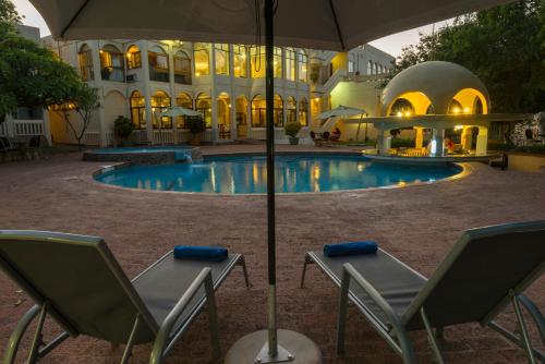 a hotel with chairs and an umbrella next to a pool at Victoria Falls Rainbow Hotel in Victoria Falls