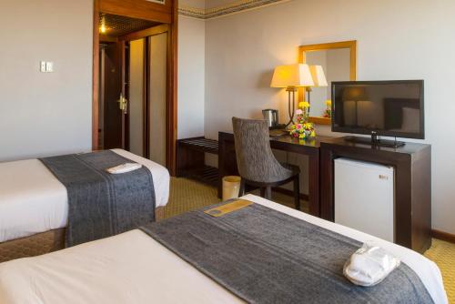 a hotel room with two beds and a desk with a television at Rainbow Towers Hotel & Conference Centre in Harare