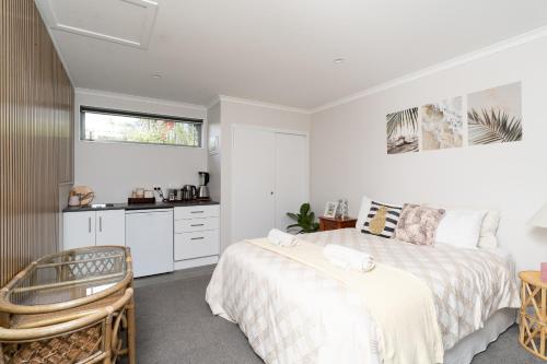 a white bedroom with a bed and a kitchen at Pineapple Palace Studio in Raglan